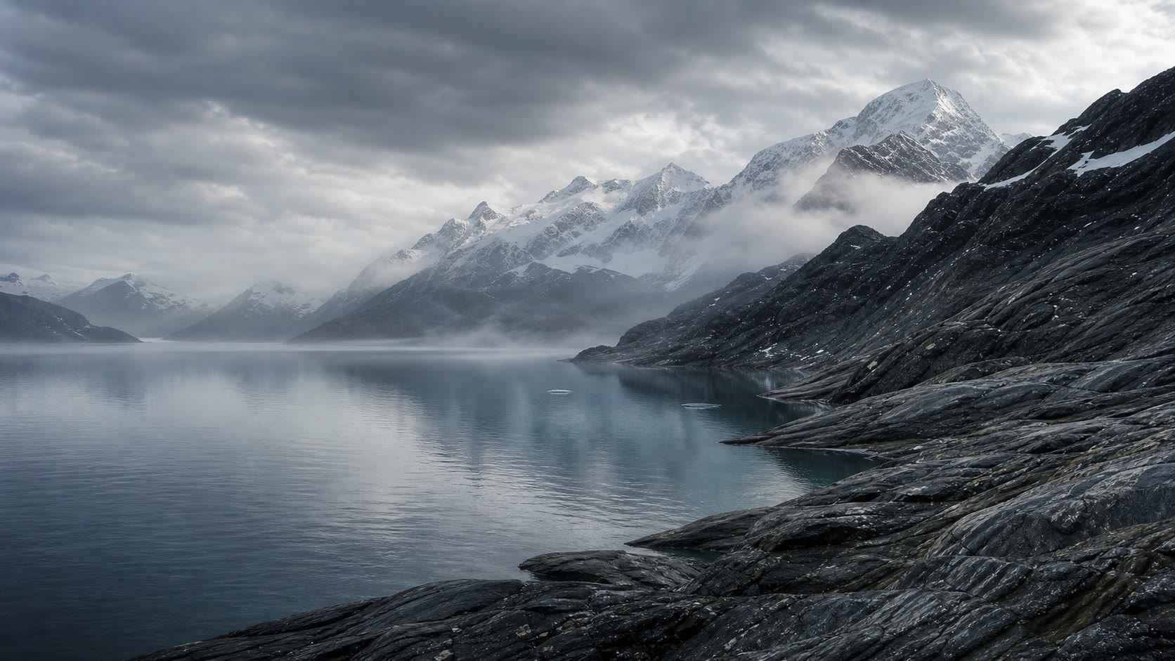 A misty alpine lake below snow-covered mountain peaks