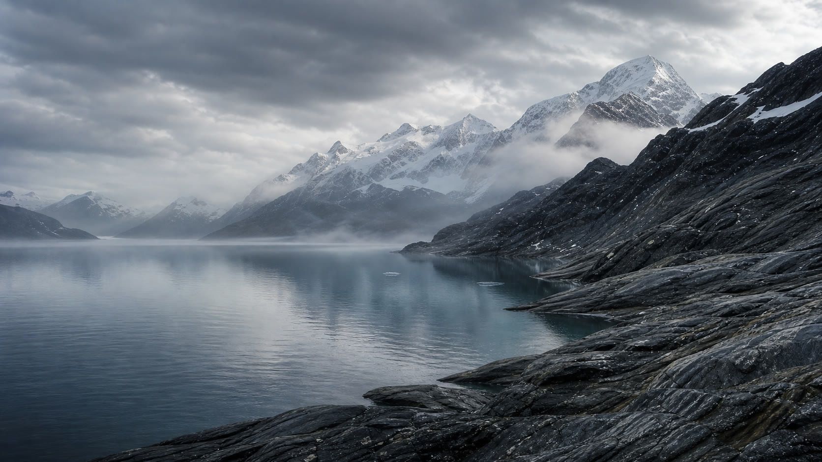 A misty alpine lake below snow-covered mountain peaks