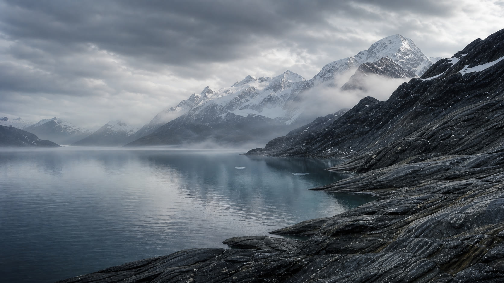 A misty alpine lake below snow-covered mountain peaks